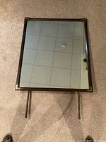 Top-down photo of rectangular mahogany mirror with brass corner accents and two mounting rods extending downwards.