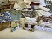 Assorted fabric remnants and upholstery pieces displayed on a bed showing different colors, patterns, and textures including floral, geometric, and solid fabrics