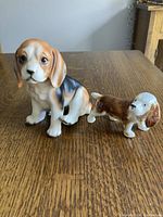 Two Beagle dog figurines shown side by side on wooden surface, larger marked Japan, smaller bone china.
