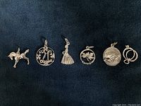 Photo showing six sterling silver charms arranged in a row on dark fabric: colt horse, 21 floral charm, bridesmaid dress, maple leaf, friendship handshake, and intertwined rings