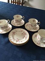 Set of 4 tea cups, 4 saucers, and 4 dessert plates arranged on tablecloth showing floral pattern and gold trim.
