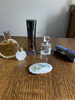 Photo showing five partial perfume bottles and embroidered lipstick holder with mirror on wooden surface