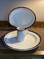 Photo showing two oval platters stacked with small jug placed on top of lower platter showing trim details and shape