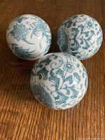 Photo showing three porcelain carpet balls placed on a wooden surface. Each ball has distinct turquoise floral pattern on a white base.