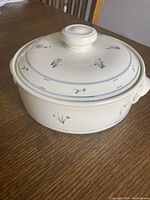 Closed cream colored ceramic casserole with blue floral designs by Priya Harding shown on wooden table.