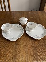 Two Royal Albert Silver Maple tea cups on matching sandwich plates with a small matching bowl on a wooden table.