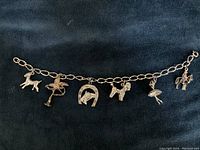 Photo of sterling silver charm bracelet with six attached charms including a poodle, ballerina, horseshoe, deer, cherub, and Mountie.