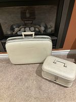 Vintage white hard shell suitcase and matching beauty case side by side on floor.