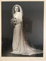 Black and white photo showing the full vintage wedding gown with long bouquet and veil, illustrating the gown's style and train length.