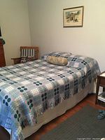 Bedspread laid flat on full/queen sized bed showing one side's geometric check and floral pattern in blue, cream, green, and other tones.