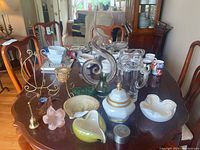 View of all items displayed on wooden dining table under daylight showing mixed art glass and porcelain items including pitcher and jar.