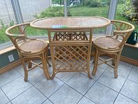 Overall view of rattan bistro set showing oval table with two matching chairs on tile floor in sunroom.