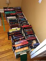 Photo showing rows of books stacked on hardwood floor with some titles visible, books organized in lines and varying in thickness and size.