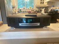 Front view of Bose Wave unit showing digital display set to 12:49 and FM 98.7, with remote on top