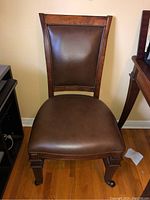 Front view of the chair showing wooden frame and brown leather padded seat and backrest.
