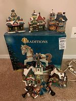 Full set of ceramic light-up Christmas village houses with carousel horse figure displayed on Traditions box.