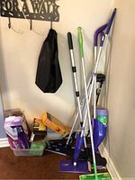 Cleaning supplies corner showing floor mops, reacher, boxes of refills, and coat rack.