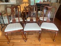 Set of six Queen Anne style dining chairs arranged in room, showing two captain chairs with armrests and four armless chairs, wooden frames and fabric seats.