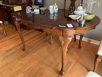 Wood dining room table with scalloped edges, carved shell accents on cabriole legs, pad feet, and polished finish. Displayed with decorative items on top.