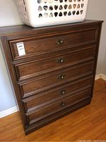 Front view of the wood dresser showing five drawers with ornate metal pulls.