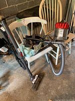 Dyson DC37 vacuum cleaner with attachments arranged on two white chairs. Dark gray canister, transparent dust container with red cyclone, flexible hose connected to wand and motorized floor head visible.