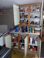 Full view of upper and lower cabinets with cleaning and laundry products, iron and ironing board to side