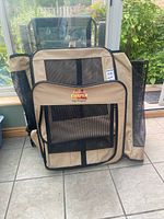 Soft sided beige fabric dog kennel with black mesh sides and front. Visible embroidered logo Canine Camper Day Tripper.