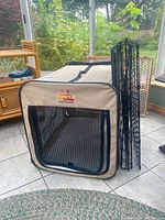 View of beige soft-sided kennel with mesh front and zippered door with separate wire frame leaning against it.