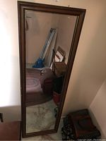 Full length mirror with wood frame standing against a wall, showing scuffs and scratches on the wood and mirror surfaces.