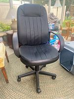 Front view of the black faux leather office chair showing padded seat, backrest with vertical stitching, and armrests.