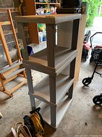 Plastic shelving unit with four shelves, grey color, showing scuffs and scratches in a garage setting.