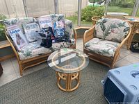 Rattan loveseat and chair with floral cushions and various items on loveseat, taken indoors on carpet.