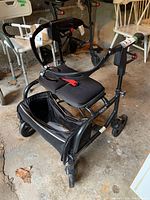 Full view of the Nexus rolling walker showing padded seat, back support, storage bag, and four wheels in garage setting.