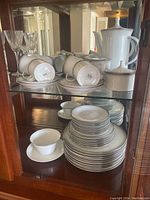 Full set displayed in a glass cabinet showing multiple cups on saucers and stacked plates on two shelves.