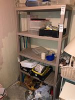 Full view of the shelving unit located in basement, holding various items which are not included in the lot, showing its four plastic shelves and general condition with scuffs and scratches.