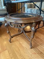 Angled view of the round carved wood side table showing ornate scrolling and female figure carvings on the legs.