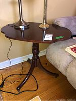 Side view of Bombay Company wooden side table on wheels next to a sofa, showing wear on finish and cords on floor.