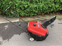 Side profile of red Honda HS520 snow blower on driveway showing auger housing, chute, and handle