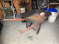 Side and top angled view of the black Jobmate wheelbarrow showing metal tray with wear and wooden handles.