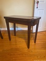 Front and side view of the dark brown wood folding table standing on a hardwood floor.