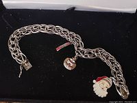 Photo of entire charm bracelet laid flat against black background, showing chain and three attached charms including Santa charm and honors charm.