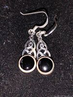 Pair of Celtic knot design earrings with round black stones on black background