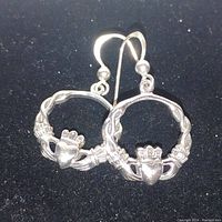 Pair of sterling silver Cladag earrings displayed on black velvet background showing front detail of heart and crown design.