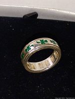 Side angle showing the entire ring, green clover inlay around the band, polished silver surface.