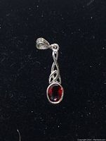 Close-up image of the oval cut red garnet pendant with Celtic knot silver design on black background.
