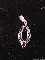 Close-up of pear shape red garnet .925 sterling silver pendant with filigree design on black background.