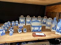 Photo of two sets of blue and white Delft-style ceramic canisters and various small kitchen and decorative items on a wooden shelf, showing detail of large and small labeled canisters, salt and pepper shakers, and figurines.