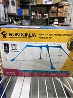 Box showing dimensions and components of Sun Ninja tent: 14ft 8in by 7ft by 7.5ft, with 4 poles, stakes, ropes, and carry bag included.