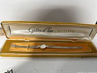 Bulova wristwatch with mesh band and round dial in open yellow velvet-lined box.