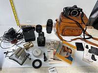 Photo of full lot including Minolta Maxxum 3000i camera body, leather case, multiple lenses and camera accessories with manuals spread on table.